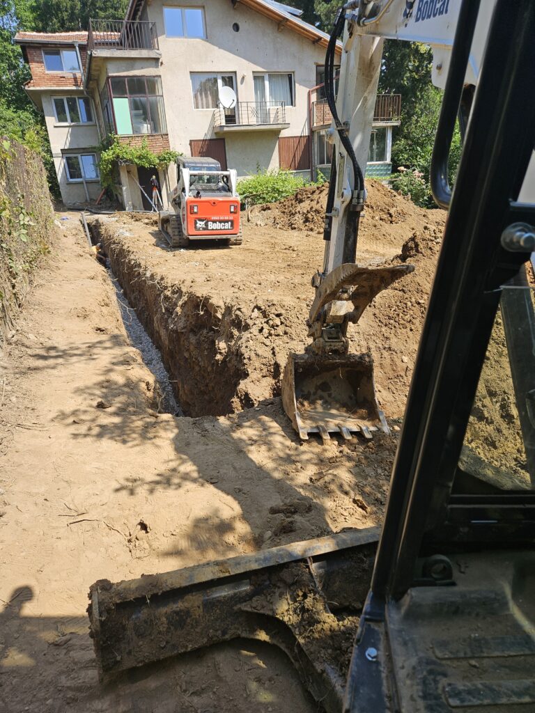 Модерен багер на PardBuild с 2D контрол копае канал за дренаж на основи на къща във Витоша.