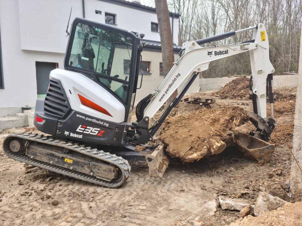 3.5-тонен багер Bobcat E35z с механичен палец извършва изкореняване на пънове в София.